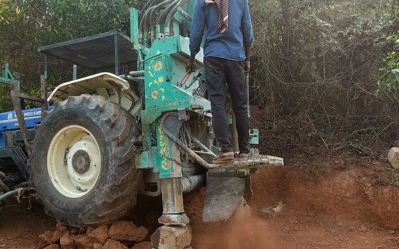 Tractor-mounted borewell drilling rig penetrating hard laterite rock with dust blowing in Iritty, Kannur